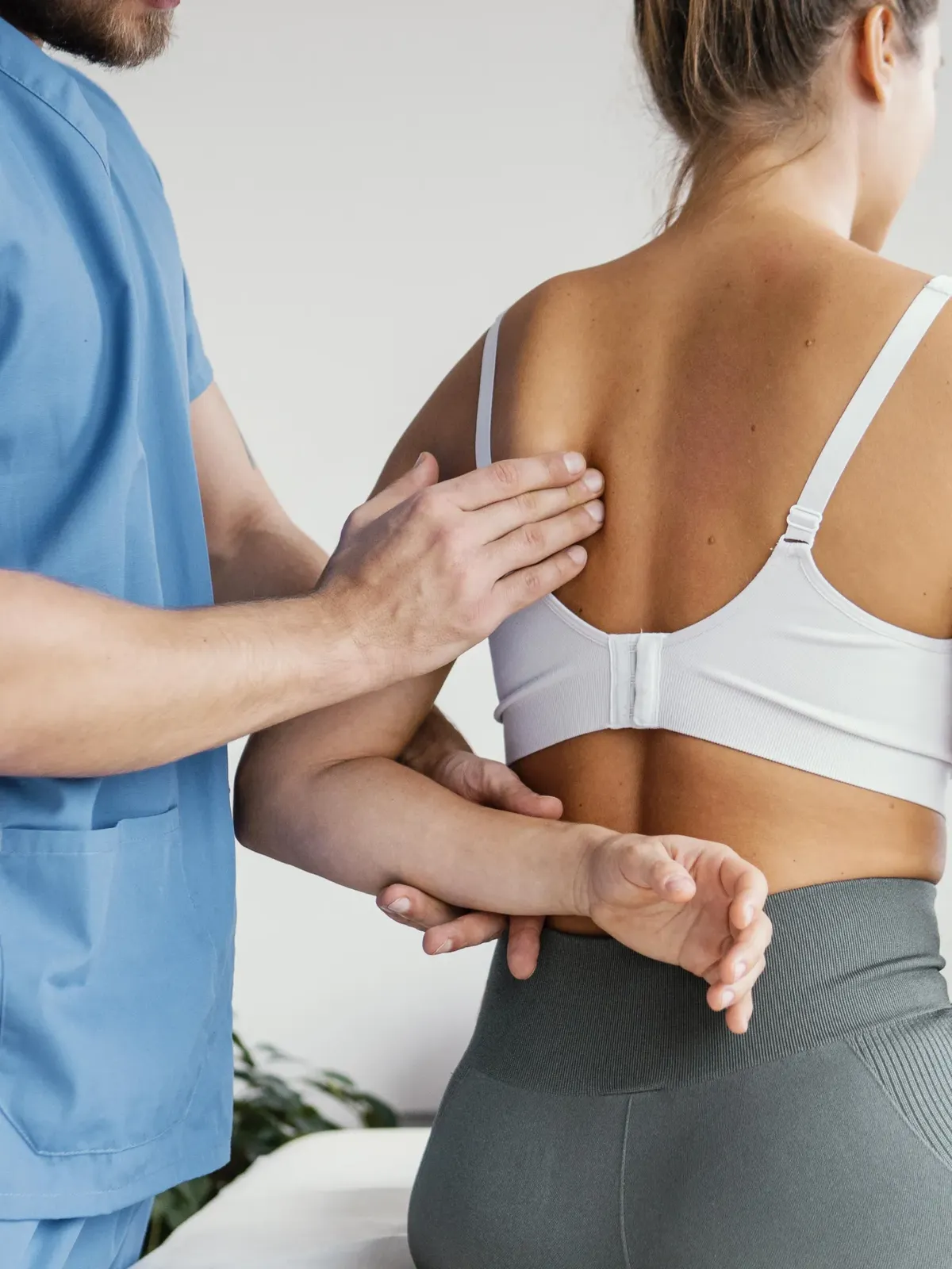 Fizjoterapeuta ocenia napięcie mięśni pleców pacjentki, stabilizując jej ramię założone za plecy