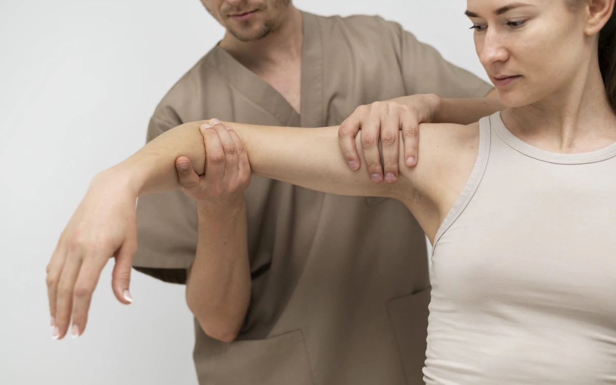 Fizjoterapeuta bada zakres ruchu w barku pacjentki, prowadząc jej uniesione ramię
